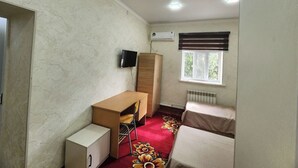 A small room with a bed, a desk, a chair, a wardrobe, an air conditioning unit, and a window with blinds.