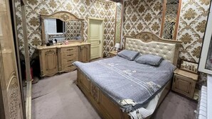 A bedroom with a large bed, a vanity with a mirror, and patterned wallpaper.