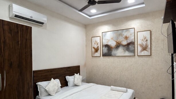 Une chambre à coucher comprenant un lit, une armoire en bois, un ventilateur de plafond, un appareil de climatisation et des œuvres d’art encadrées accrochées au mur.