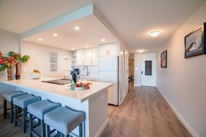 Una cocina moderna con armarios blancos, una isla central con taburetes y un refrigerador.