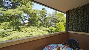 Un balcón con una mesa para dos, vistas a un jardín exuberante y un muro de piedra.