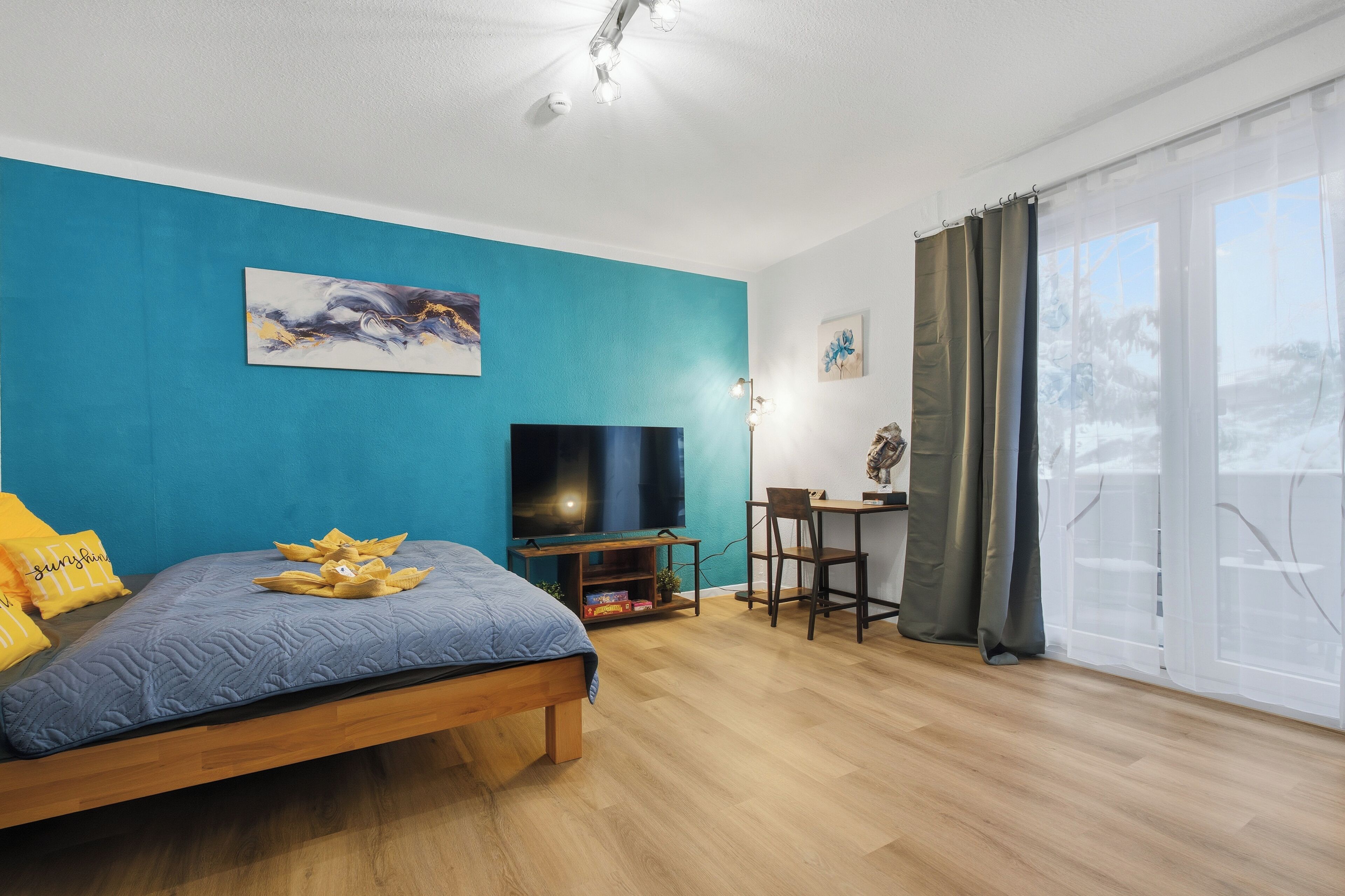 Ein modernes Zimmer mit einem Bett, einem Schreibtisch, einem Fernseher und einem großen Fenster mit Vorhängen.