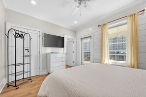Une chambre à coucher avec un grand lit, une armoire, un téléviseur fixé au mur et une fenêtre avec des rideaux.