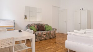 Ein Zimmer mit einem weißen Bett, einem blumigen Sofa, einem weißen Tisch und einem Kleiderschrank.