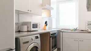 Eine kleine Küche mit Waschmaschine, Mikrowelle, Backofen und einem Fenster für natürliches Licht.