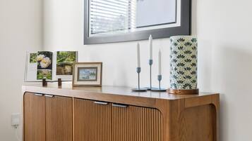 Una consola de madera con un cuadro enmarcado, velas y objetos decorativos frente a una pared blanca.