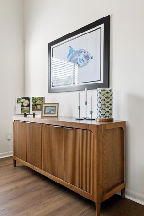 Una consola de madera con un cuadro enmarcado, velas y objetos decorativos frente a una pared blanca.