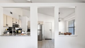 A modern kitchen with white cabinets, a stainless steel refrigerator, and a dining area with a window.