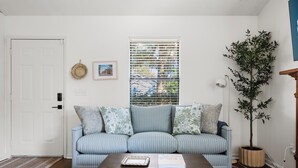 A living room with a striped sofa, a coffee table, a potted plant, and a window with blinds.