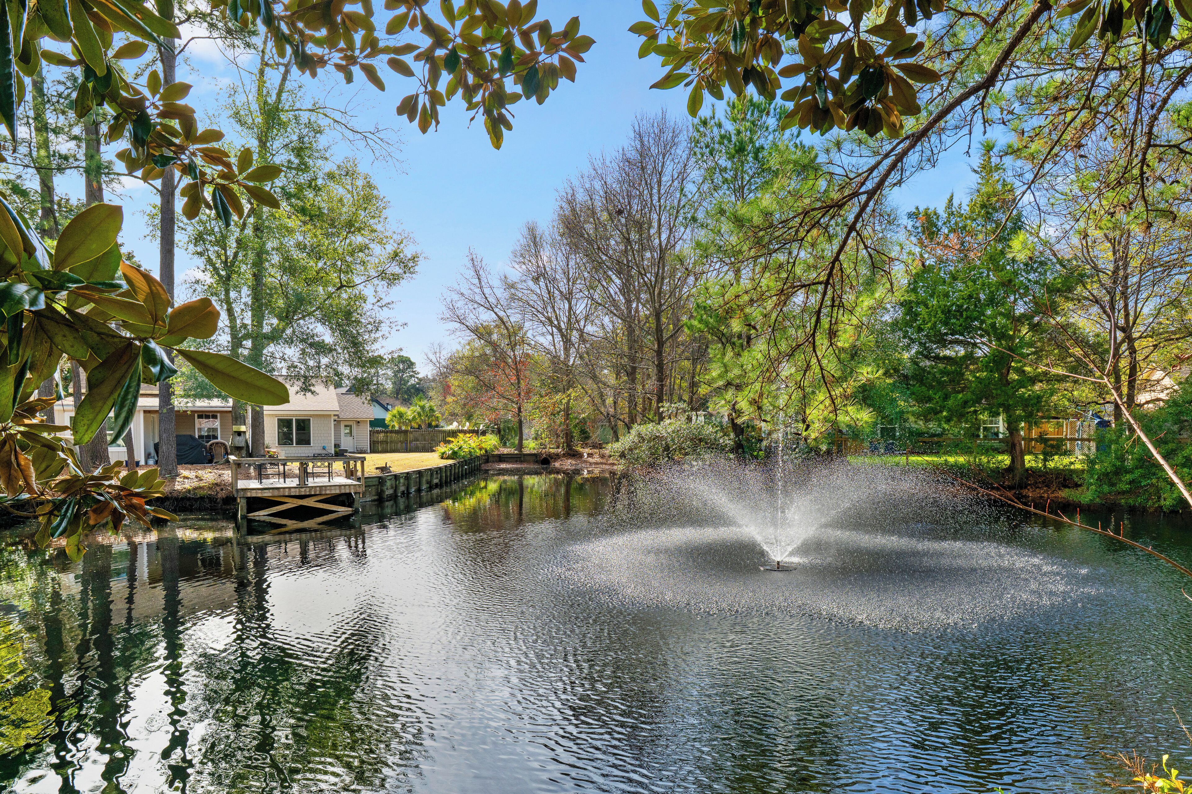 A tranquil pond with a fountain, surrounded by lush greenery and a wooden dock.