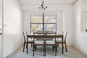 Ein Esszimmer mit Tisch und Stühlen, einer Kandelaber und einem Fenster mit Jalousien.