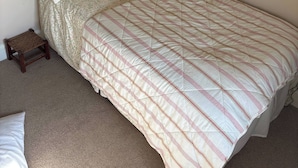 Una cama individual con cabecera de madera, una colcha acolchada y un taburete de madera.