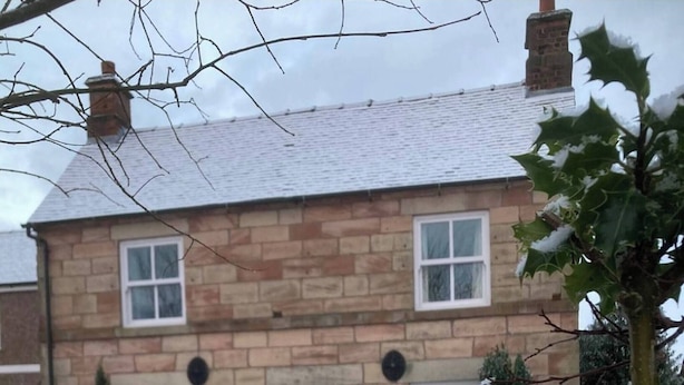 Una casa de piedra de dos plantas con fachada simétrica, varios ventanales y un jardín cubierto de nieve.