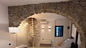 A modern interior with a stone archway, a spiral staircase, a sofa, a chair, and a fireplace. - Villa Olive Mill Terra Rossa  (Corniglia)