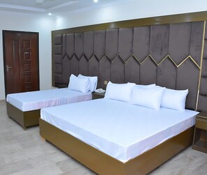 A hotel room with two single beds, a wooden door, and a padded headboard. - New Maharaja Hotel (Rawalpindi)