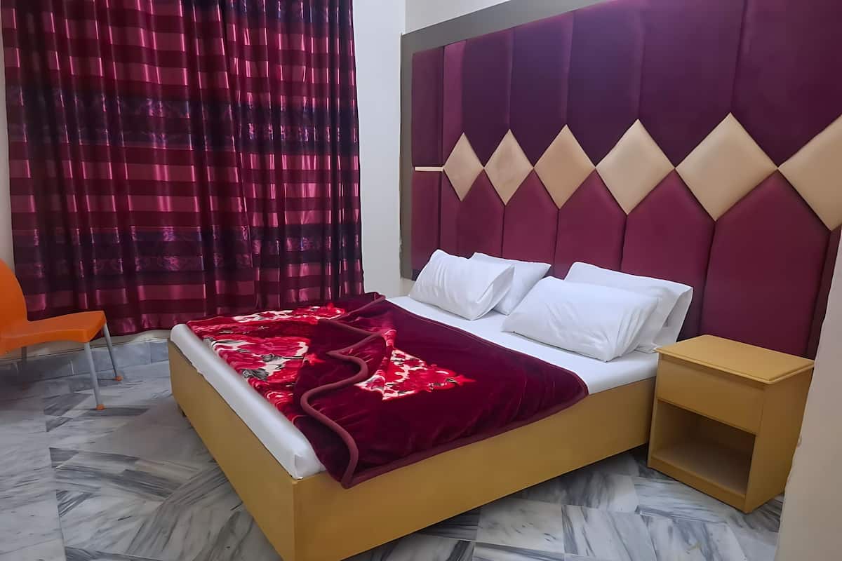 Een bed met een rood-witte dekbedovertrek, een hoofdbord met diamantmotieven, en een nachtkastje.