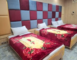 A hotel room with two beds, each with a floral bedspread and white pillows. The headboard is padded with a checkered pattern of red and blue.