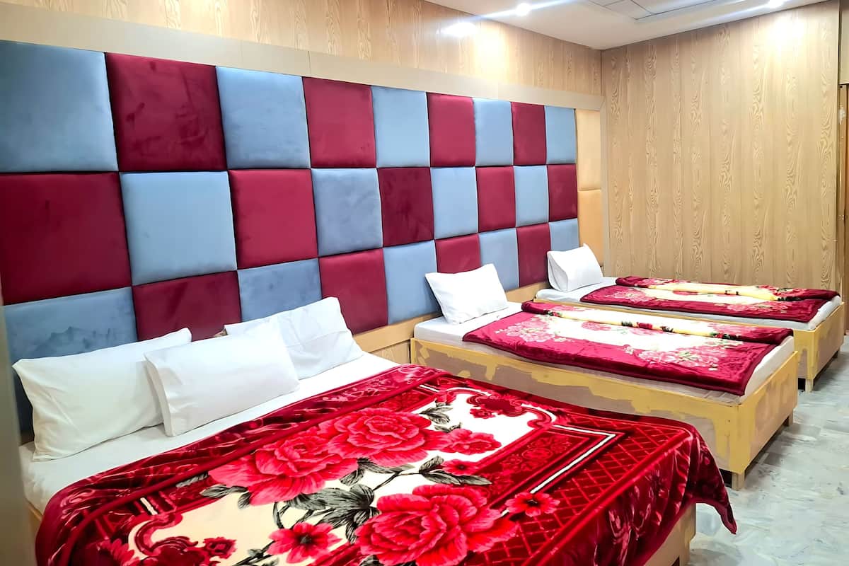 Een hotelkamer met een groot gestoffeerd hoofdeinde, twee bedden met bloemenbeddels, en een wand van houten panelen.
