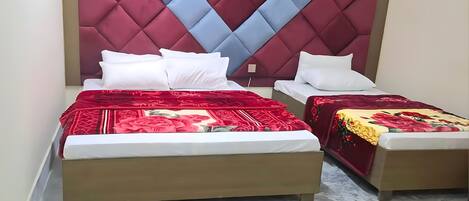Habitación de hotel con dos camas, cada una con una colcha floral roja y amarilla. La habitación tiene un piso de mármol y un cabecero grande con estampado de diamantes.