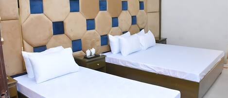 A hotel room with two beds, a wooden headboard with a geometric pattern, and a nightstand with a lamp.