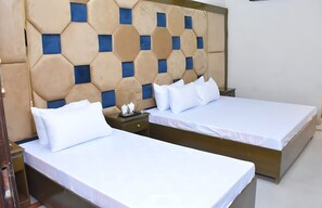 A hotel room with two beds, a wooden headboard with a geometric pattern, and a nightstand with a lamp. - New Maharaja Hotel (Rawalpindi)