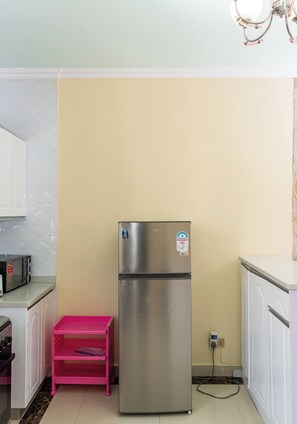 A kitchen with a stainless steel refrigerator, a pink plastic shelf, and a white countertop. - State House Haven 3 Bedroom Suite (Nairobi)