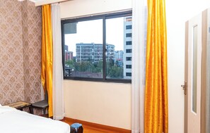 A hotel room with a large window, a bed, a small table, and a chair. - State House Haven 3 Bedroom Suite (Nairobi)