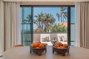 A dining table with two bowls of fruit in a room with large windows overlooking palm trees and a building. - Villa Mangoni - Brand New Luxury Villa (Funchal)