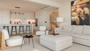 Una sala de estar moderna con un sofá blanco, una mesa de centro y un comedor con taburetes de bar.