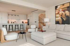A modern living room with a white sofa, a coffee table, and a dining area with bar stools. - Villa Mangoni - Brand New Luxury Villa (Funchal)