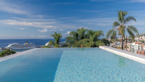 Una piscina infinita de color azul intenso con vistas al océano y un crucero a lo lejos.
