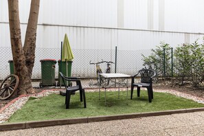 A small outdoor seating area with two chairs and a table, surrounded by a chain-link fence, a bicycle, and a trash bin. - Affordable Private Room Easy City Access (Vienna)