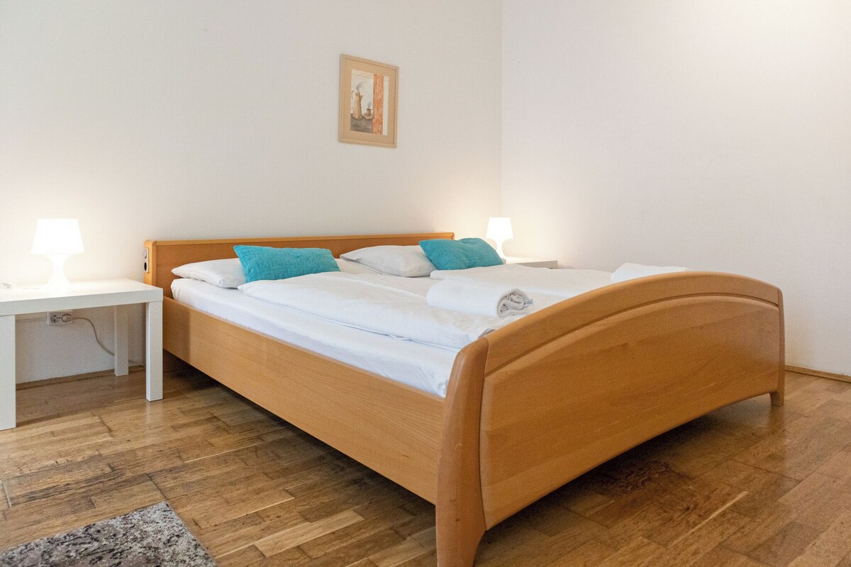 Ein Einzelbett mit Holzrahmen und weißer Bettwäsche, zwei Nachttische mit Lampen, ein kleiner Teppich und ein gerahmtes Bild an der Wand.