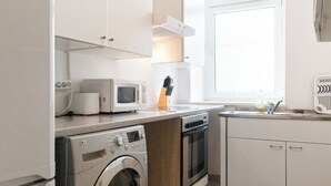 Eine kleine Küche mit Waschmaschine, Mikrowelle, Backofen und einem Fenster für natürliches Licht.