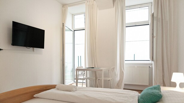 Ein Hotelzimmer mit Bett, Schreibtisch, Stuhl, Fernseher und einem fenster mit Vorhängen.