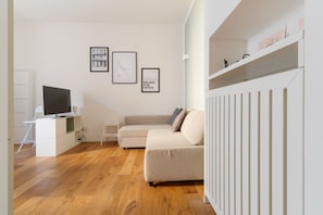 Ein modernes Wohnzimmer mit einer Couch, einem Fernseher auf einem Schrank, einer Heizung und gerahmten Kunstwerken an der Wand.