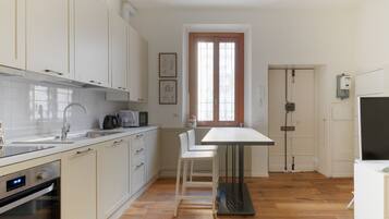 Eine moderne Küche mit weißen Schränken, einer Edelstahlspüle, einem eingebauten Backofen und einem Essbereich mit Tisch und zwei Stühlen.