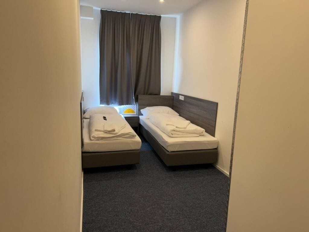 Ein kleines Hotelzimmer mit zwei Einzelbetten, einem Fenster mit Vorhängen und Teppichboden.