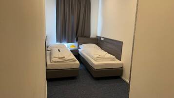 Ein kleines Hotelzimmer mit zwei Einzelbetten, einem Fenster mit Vorhängen und Teppichboden.