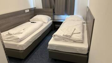 Quarto pequeno com duas camas de solteiro, cada uma com cabeceira de madeira e roupa de cama branca.