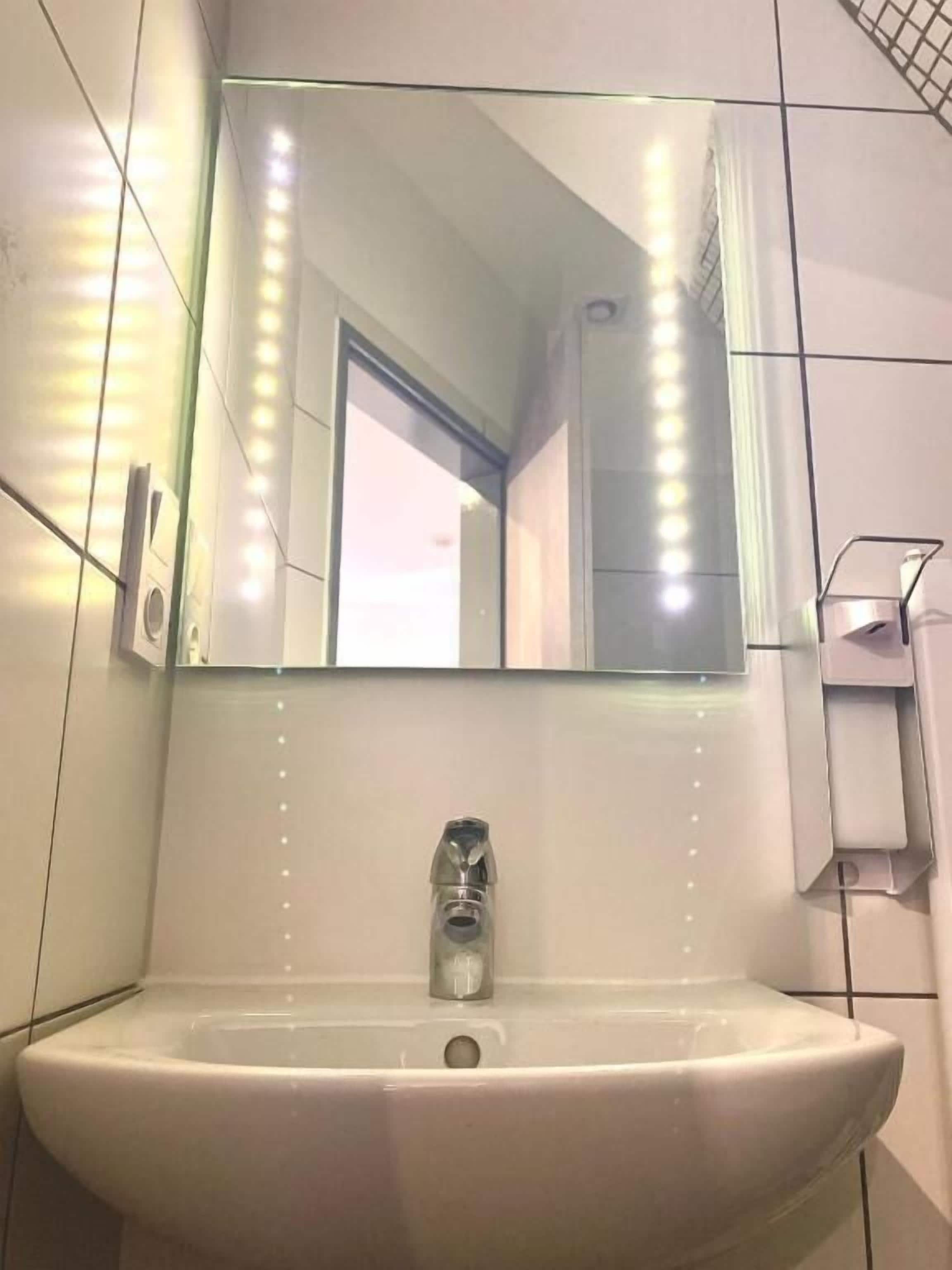 A bathroom with a white sink, a mirror, and a towel dispenser.