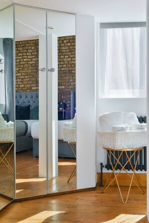 Ein Zimmer mit einem raumhohen Spiegelkleiderschrank, einer Ziegelwand, einer Couch, einem weißen Stuhl und einem Heizkörper.