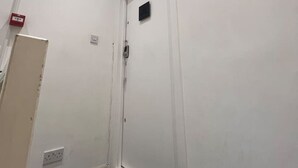 Een witte deur met een klein raam, een lamp aan het plafond en een stopcontact op de muur.
