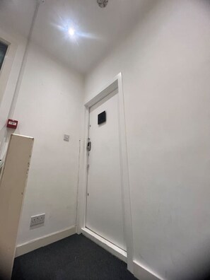 Eine weiße Tür mit einem kleinen Fenster, einer Leuchte an der Decke und einer Steckdose an der Wand.
