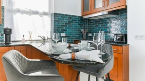 Een moderne keuken met een eethoek, voorzien van een zwart aanrechtblad, houten keukenkastjes en een blauwgroene spatwand.