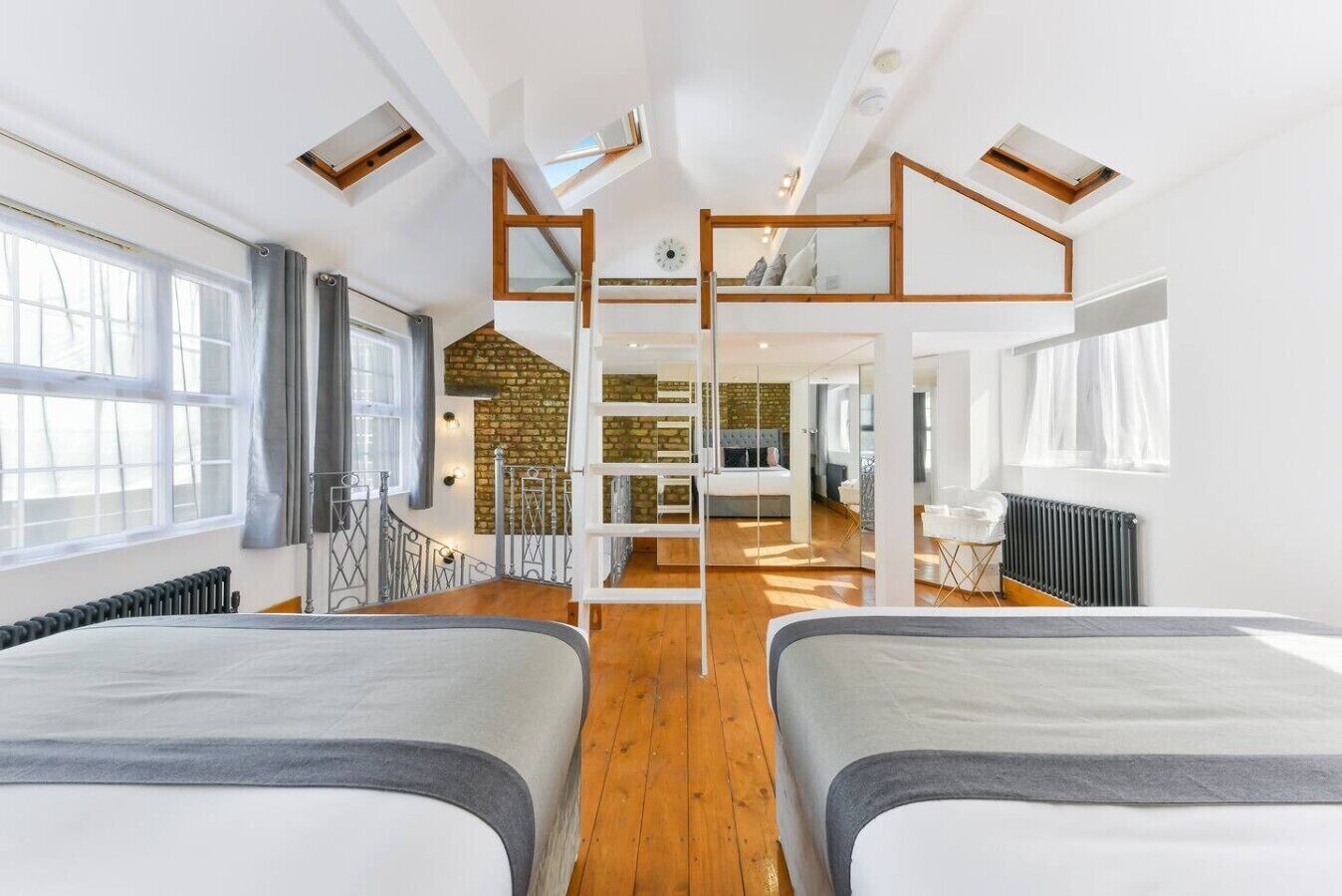 Habitación de hotel moderna con dos camas, una pared de ladrillo y un altillo con escritorio y silla.