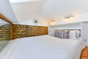 Ein Schlafzimmer mit Backsteinwand, einem Bett mit gemusterten Kissen, einer Uhr und integrierter Beleuchtung.