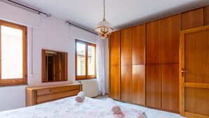 A bedroom with a bed, wooden wardrobe, a dresser, a mirror, and a window with curtains.