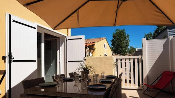 An outdoor patio with a table set for dining, a red lounge chair, and a white fence. - House in Vias-plage Near Sandy Beach (Vias)