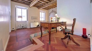 Una stanza con soffitto in legno, una scrivania con cassetti, una sedia, un termosifone e una finestra.